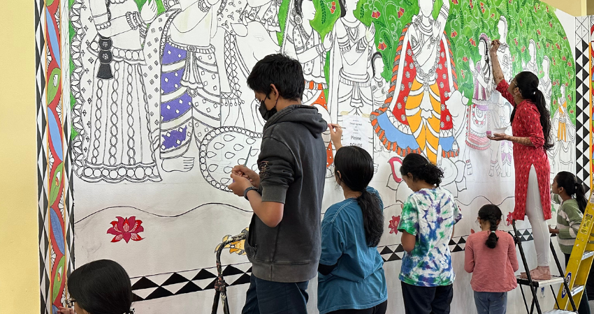 Students work together to paint a large wall mural in the Madhubani style.