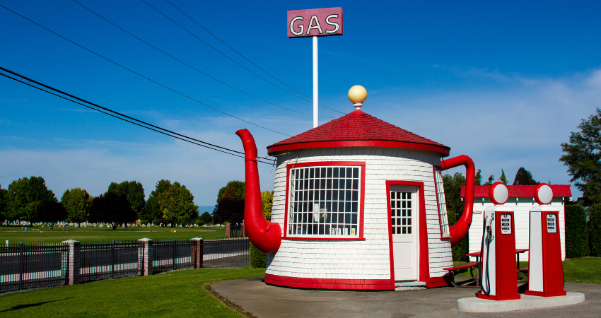 Photograph of the Teapot Dome Service Station located in Zillah, WA: a white and red building in the shape of a teapot, complete with spout and handle. A sign sticks out of the top reading "GAS".